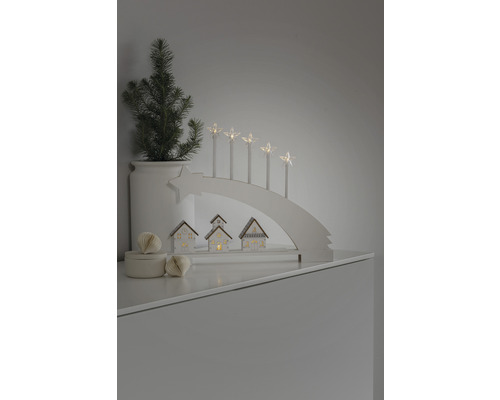 Dekorativ julscen med ljusbåge, stjärnljus, små hus och en krukväxt.