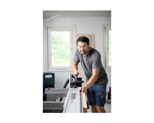 En man sågar en träbräda med en handsågcirkelsåg på en styrskena, medan han bär skyddsglasögon.