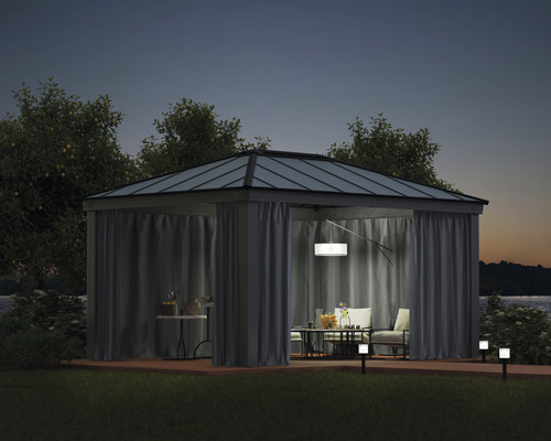 Paviljong med gardiner, bord och stolar på en terrass på natten