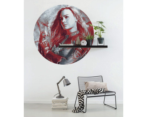 Väggdekoration med Captain Marvel-motiv ovanför en hylla med dekorationer, lampa och stol i rummet.