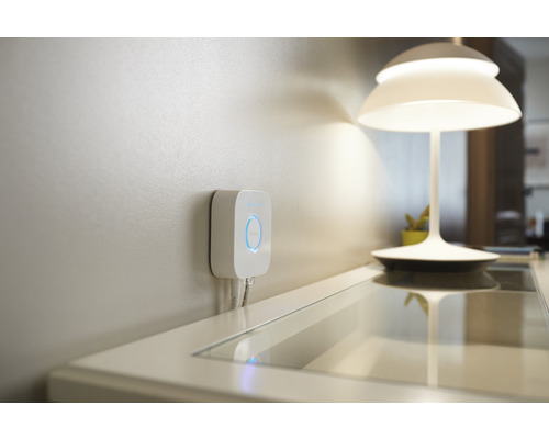Philips Hue Bridge för att styra smart hem-belysning monterad på väggen, bredvid en bordslampa.