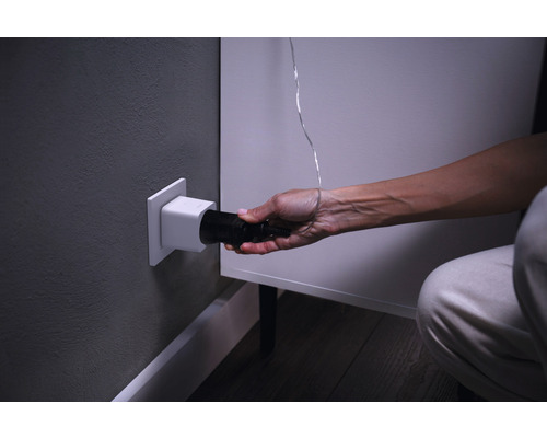 En person sätter in en svart kontakt i ett vitt vägguttag.