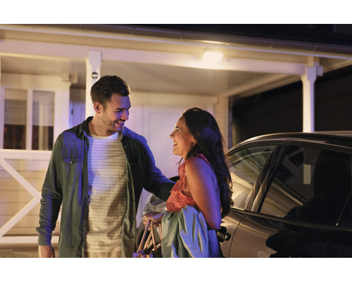 Ett par skrattar framför ett hus och en bil.