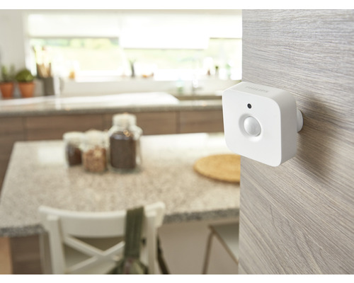 Vit Philips Hue rörelsesensor monterad på en ljus träyta i ett ljust, organiserat kök.