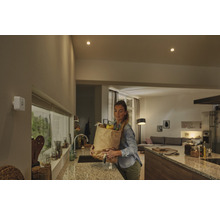 Vit rörelsesensor på en vägg i ett modernt kök med en kvinna som bär en matkasse.