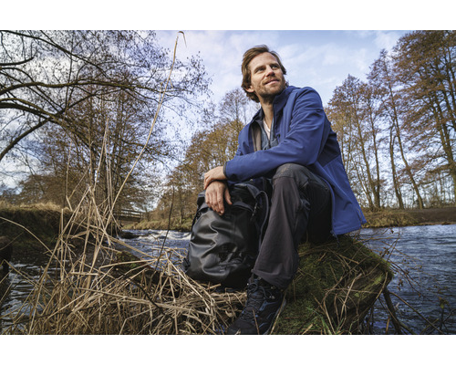 Man med ryggsäck sitter vid floden i naturen