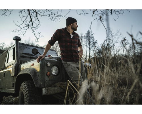 Man i rutig skjorta lutar sig mot en terrängbil i en naturnära miljö