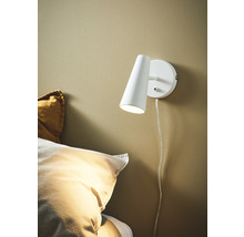 Vit vägglampa bredvid en säng
