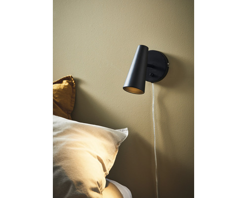 Svart vägglampa med sladd bredvid en säng
