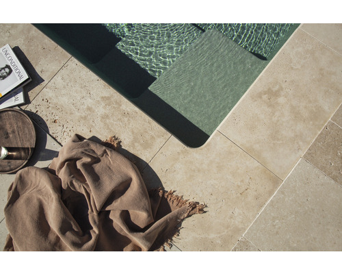 Detaljvy av en pool med naturstensplattor, en bok, en dryck och en handduk