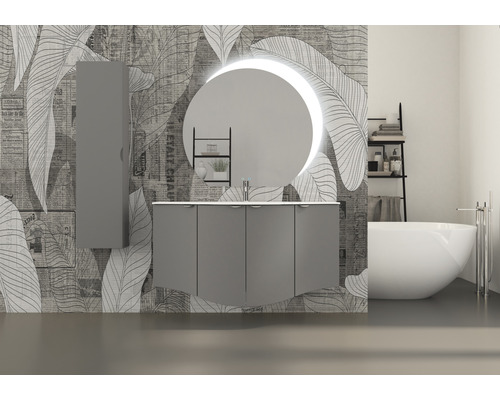 Badrum med tvättställsskåp, spegelskåp, rund spegel med belysning och badkar framför en mönstrad vägg