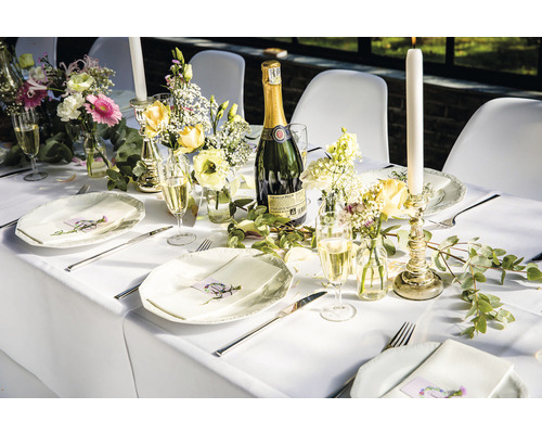 Dukat bord med tallrikar, bestick, glas, blommor, ljus och en flaska mousserande vin för en fest