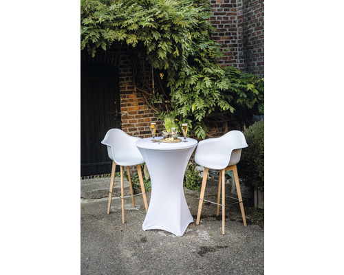 Ståbord med stretchöverdrag och barstolar framför en tegelvägg med växter