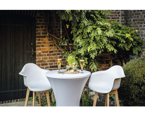 Utomhusscen med ståbord, två stolar, drycker och snacks framför en tegelvägg och växter.