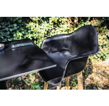 Svart trädgårdsstol och bord med bestick utomhus.