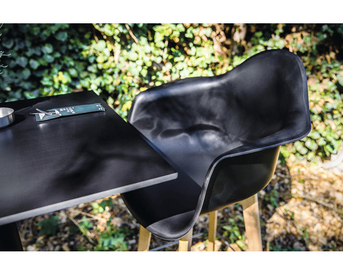 Svart trädgårdsstol och bord med bestick utomhus.