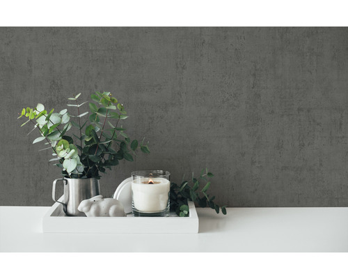 Dekorativ scen med ljus, växt och dekorativ figur på en bricka framför en vägg.