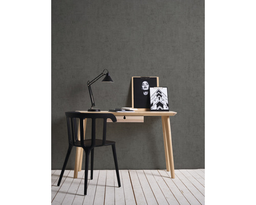 Skrivbord med låda, skrivbordslampa och svart stol mot en grå vägg