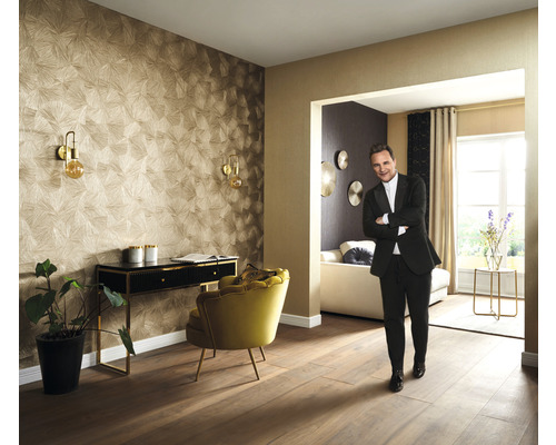 Vardagsrum med mönstrad tapet, skrivbord, fåtölj och en person