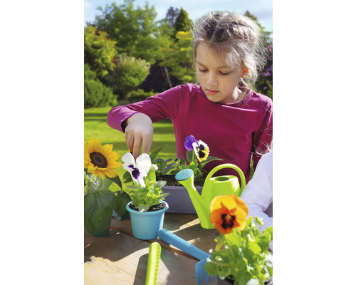 Flicka planterar blommor i trädgården med vattenkanna och trädgårdsredskap