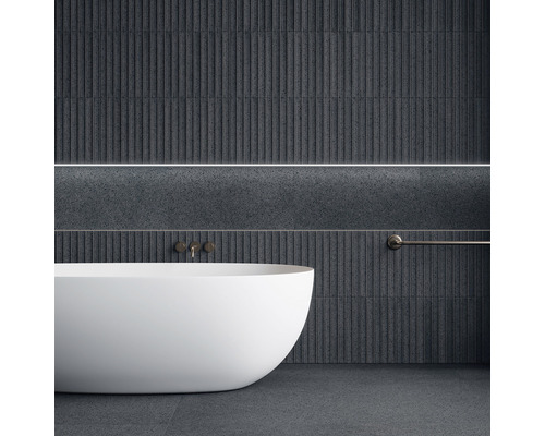 Badrum med fristående badkar, armatur och handdukshängare mot mörka väggplattor