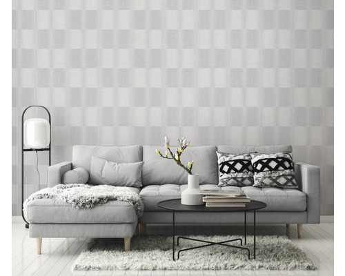 Ljust vardagsrum med grå soffa, bord och mönstrad tapet för en vänlig atmosfär.