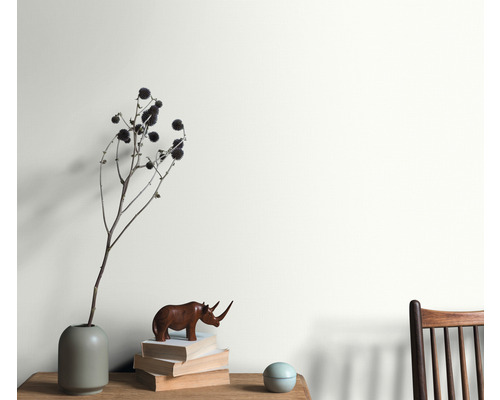 Vardagsrum med arrangemang av vas, dekorationsobjekt och stapel med böcker framför en målad vägg.