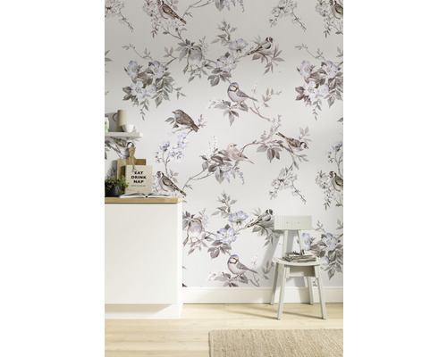 Rum med tapet med fågel- och blomstermotiv, ett vitt skåp och en stol.