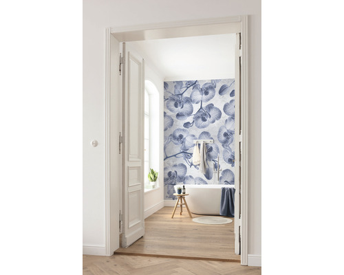 Ljust badrum med badkar, trägolv och fototapet med orkidémönster, fotograferat genom en öppen dörr.