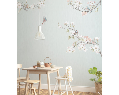 Matsal med ljust träbord, stolar, pall, porslin, krukväxt och en väggtapet med fågel- och blommotiv.