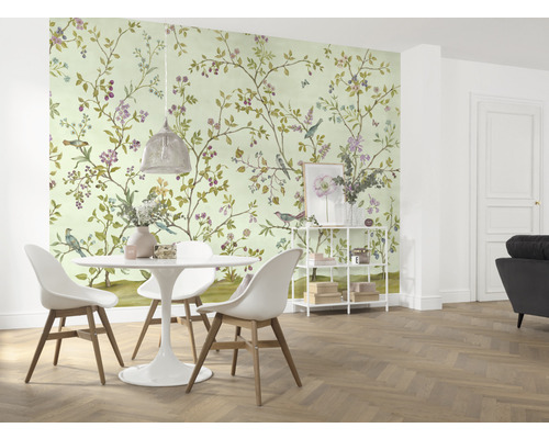 En matsal med en tapet med fågel- och blomstermönster, ett matbord och stolar.