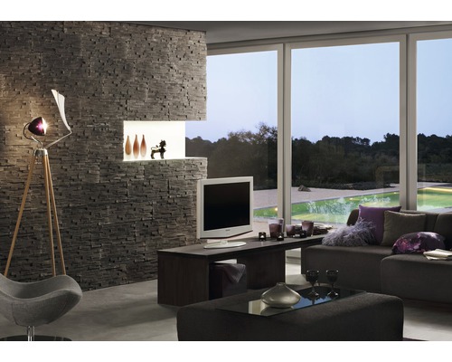 Vardagsrum med stenvägg, TV, lampa och fönsterparti med utsikt mot grönska