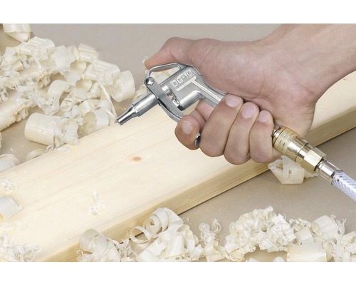 Tryckluftpistol i handen bredvid träbräda och träspån