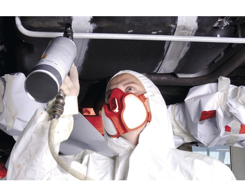 En person i skyddskläder sprayar underredsskydd på en bil.