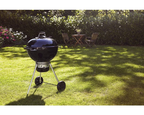Klotgrill på gräsmatta i trädgården med bord och stolar i bakgrunden