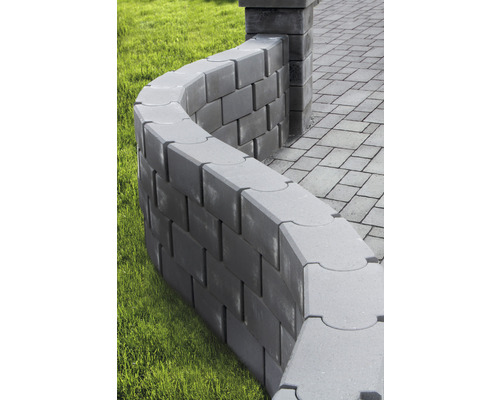 Svängd trädgårdsmur av betongblock bredvid en asfalterad gångväg