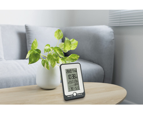 Väderstation på ett bord med växt och soffa i bakgrunden