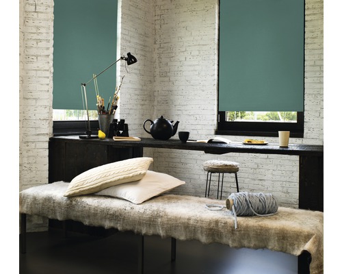 Ljust rum med två fönster utrustade med rullgardiner, en bänk och ett skrivbord med dekorativa föremål