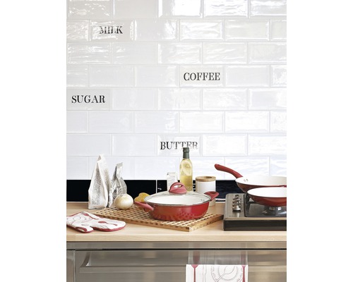 Köksscen med kastrull, stekpanna och köksredskap framför en vit kakelvägg