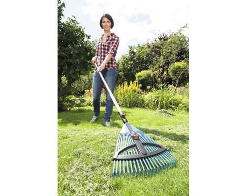 En kvinna använder en lövrake i trädgården för att kratta gräs.