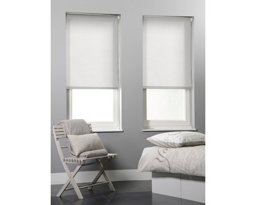 Två vita rullgardiner på fönster i ett sovrum med en stol och en säng