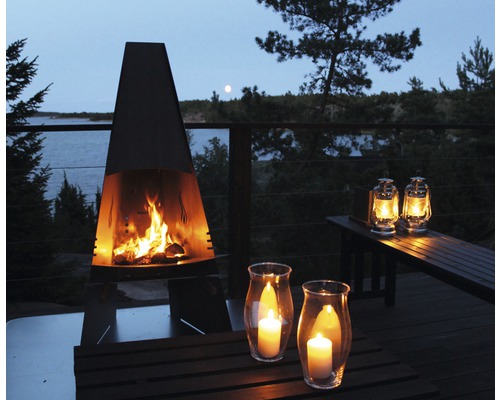 Atmosfärisk trädgårdsscen med utomhuseldstad, lyktor och ljuslyktor på en träterrass vid en sjö.