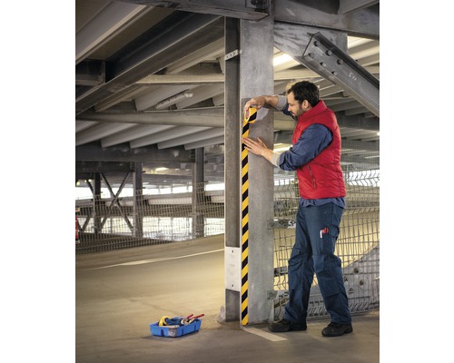 Man fäster påkörningsskydd på en stolpe i ett garage.