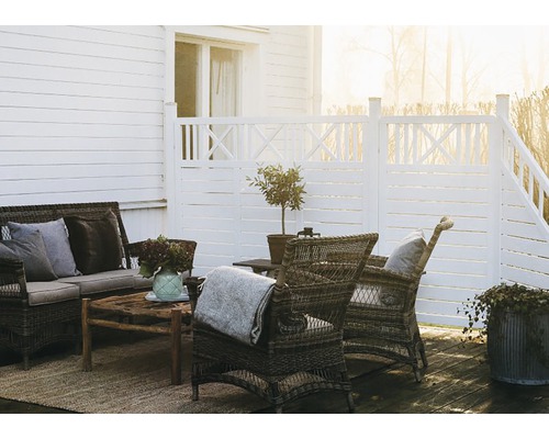 Terrass med vita trästaket, rotting sittgrupp och träbord på en matta.