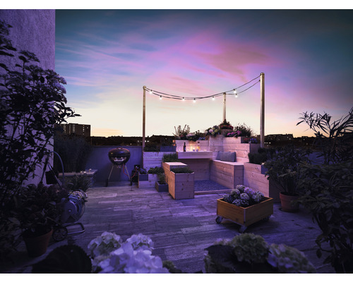 Takterrass med grill, trämöbler, planteringar och ljusslinga i skymningen