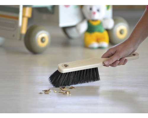 Handborste med trähandtag och mörka borst sträcker sig över golvet.