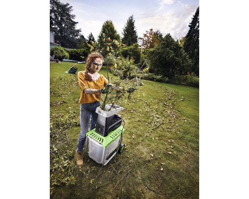 Kvinna använder en elektrisk trädgårdshack för att strimla grenar