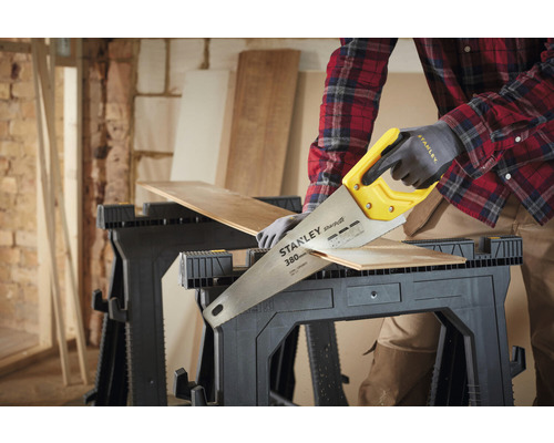 En person sågar en bit trä på två bockar med en handsåg från Stanley.