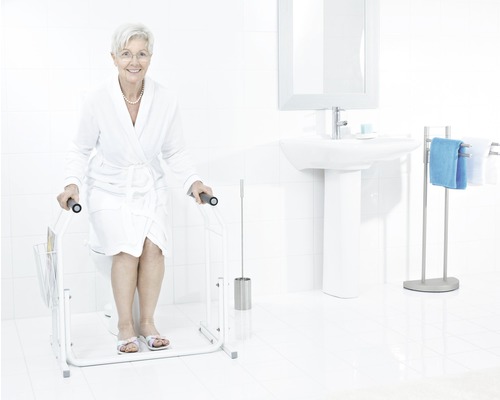 Ljust badrum med toalett, handfat och en äldre kvinna som använder ett toalettstöd