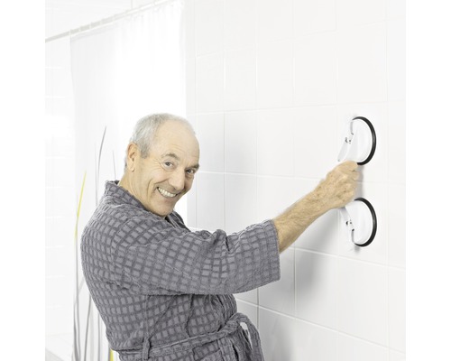 En man i badrock fäster ett handtag med sugproppar på en kakelvägg.